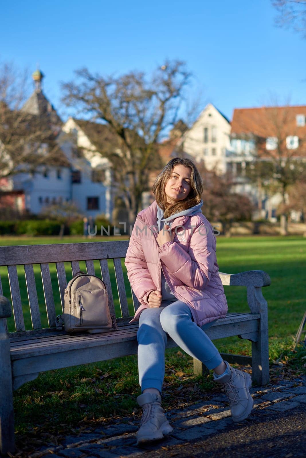 Winter Joy in Bitigheim-Bissingen: Beautiful Girl in Pink Jacket Sitting Amidst Half-Timbered Charm. beautiful girl in a pink winter jacket sitting on a bench in a park, set against the backdrop of the historic town of Bitigheim-Bissingen, Baden-Württemberg, Germany. by Andrii_Ko