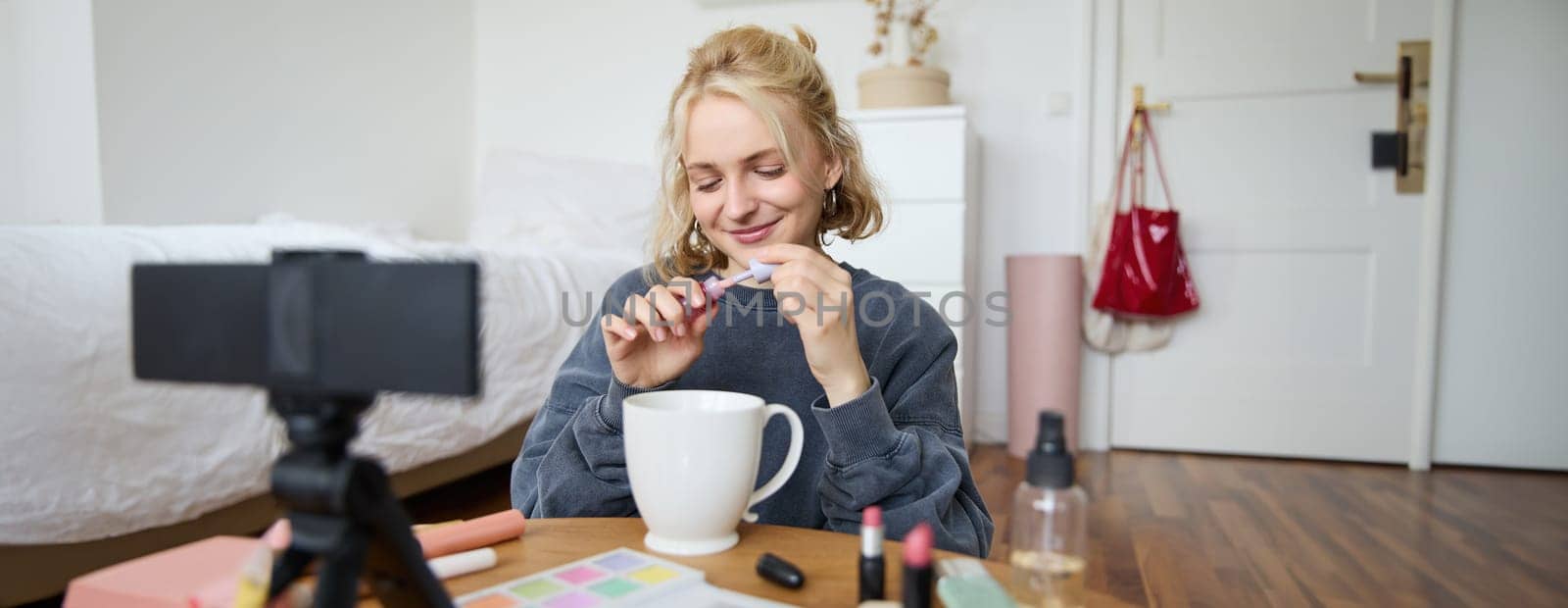 Image of happy, beautiful young social media influencer, female vlogger records a video on digital camera, tutorial on how to put makeup, getting ready for going out, talking to followers.