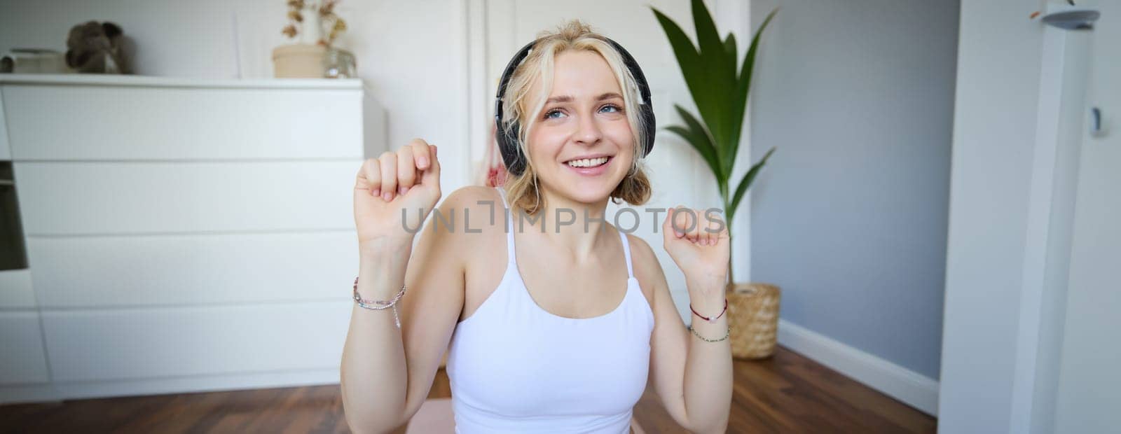 Close up of athletic young woman, cute female model in wireless headphones, dancing to favorite song, listens to music in earphones.