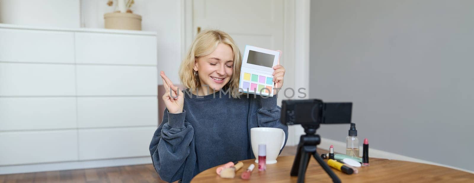 Portrait of beautiful lifestyle blogger, girl records a video on her camera for social media, shows palette of eyeshadows, does a makeup tutorial for her followers, sits in her room.