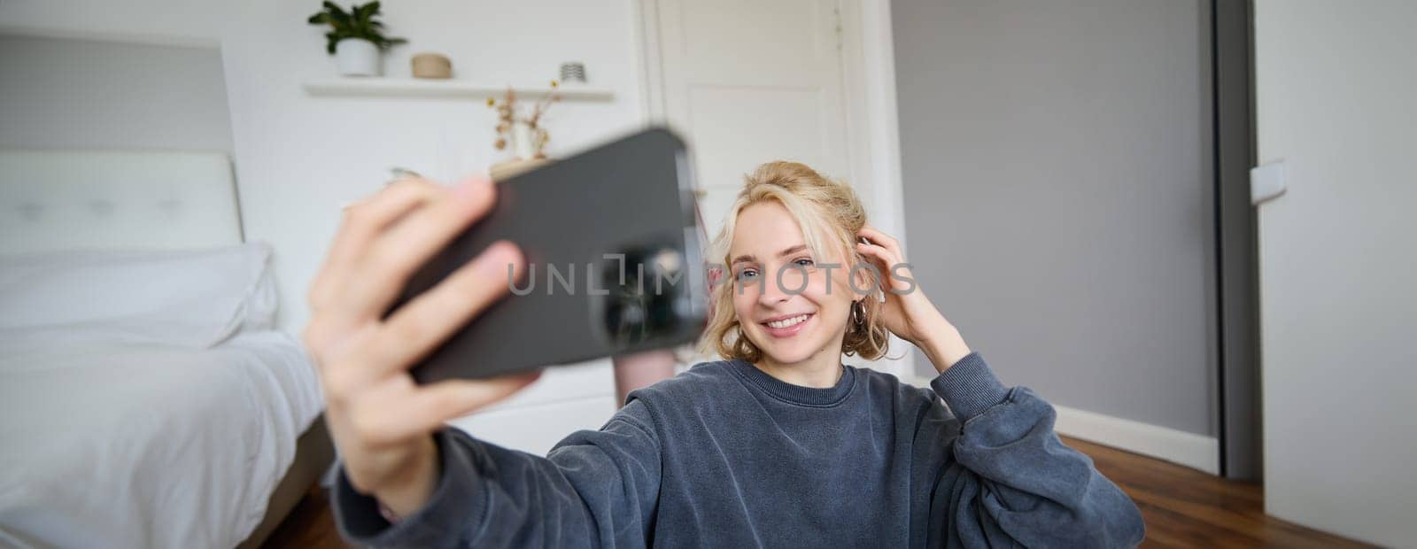 Portrait of young woman, social media influencer, taking selfies in her room, sitting on floor, holding smartphone and posing for a photo by Benzoix