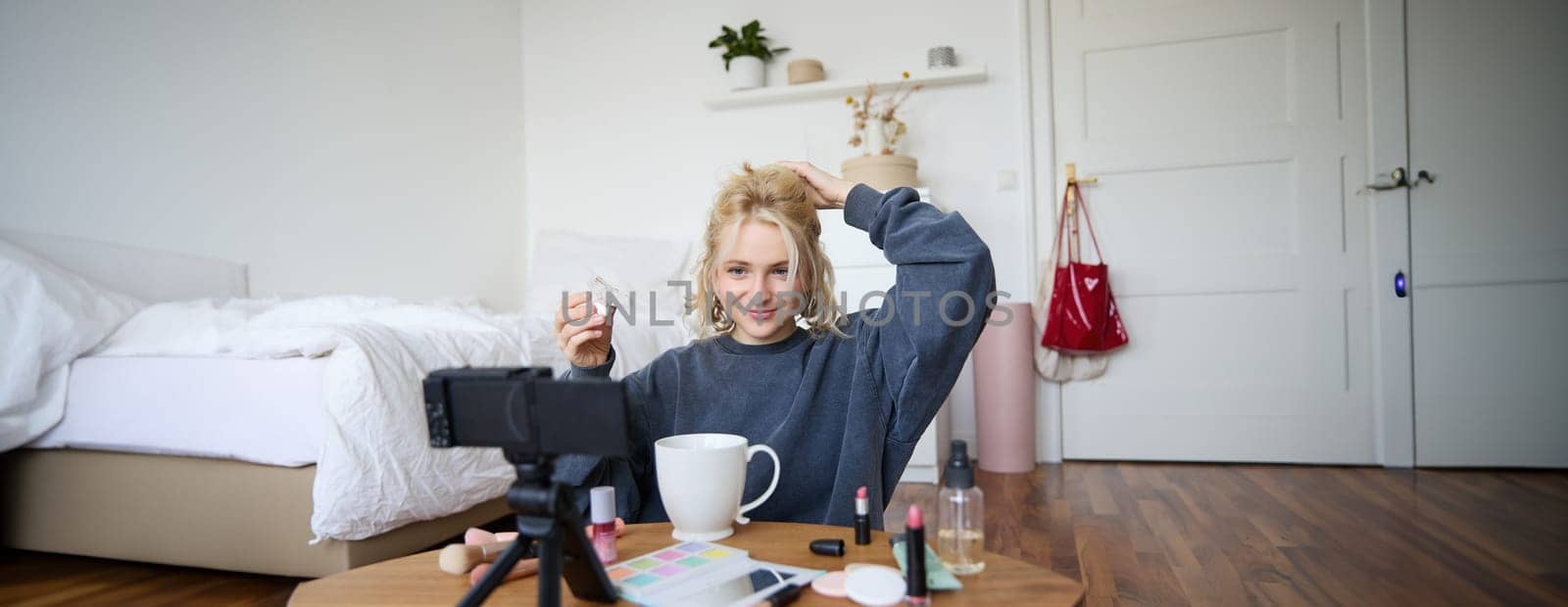 Portrait of stylish, smiling beautiful woman, recording lifestyle vlog, getting ready on camera, showing how to make her hairstyle for social media followers, vlogging from her room.