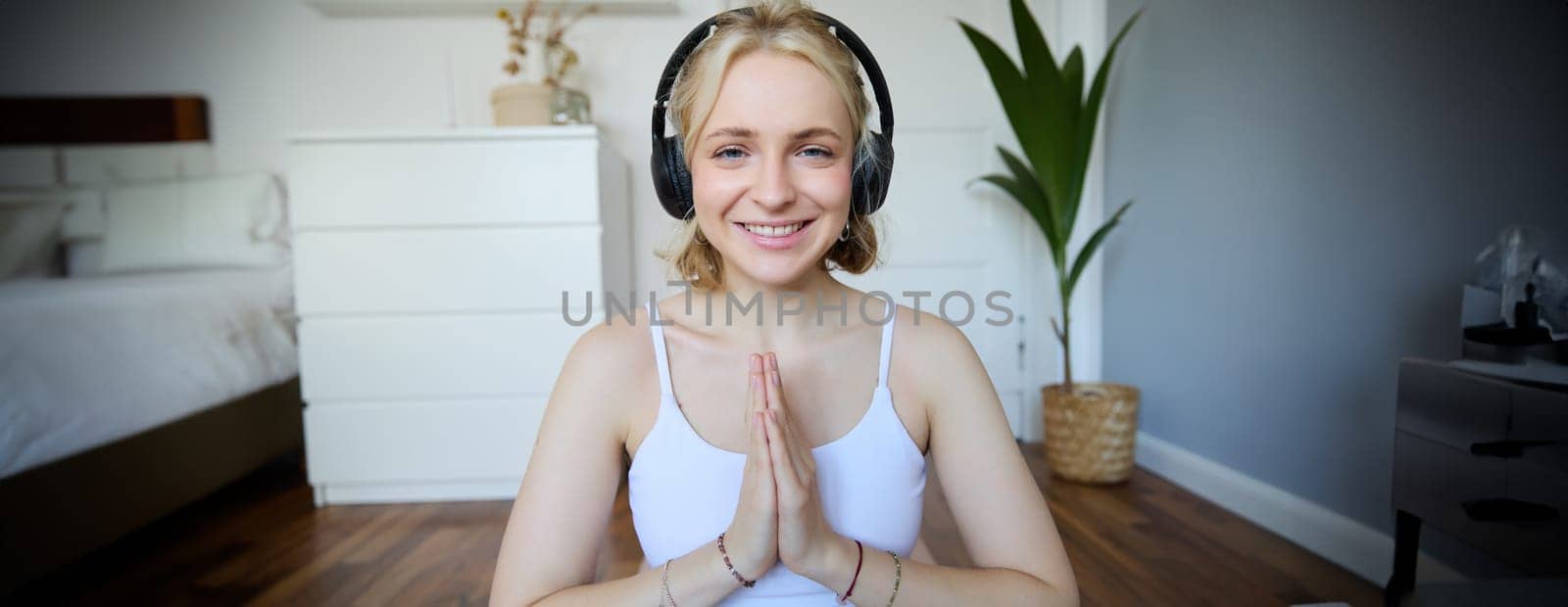 Wellbeing and people concept. Close up portrait of young woman in headphones, meditating, practice yoga, listens to podcast in earphones by Benzoix