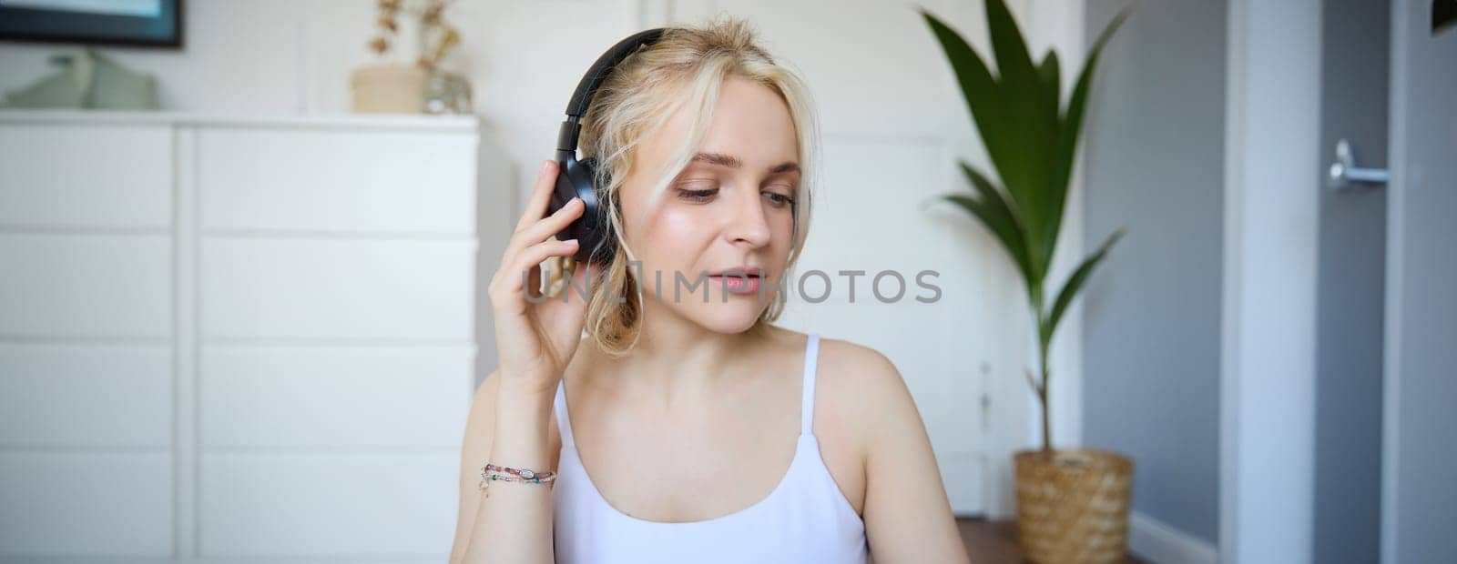 Portrait of good-looking young blond woman in wireless headphones, listens to podcast or favourite song, enjoys music in new earphones by Benzoix