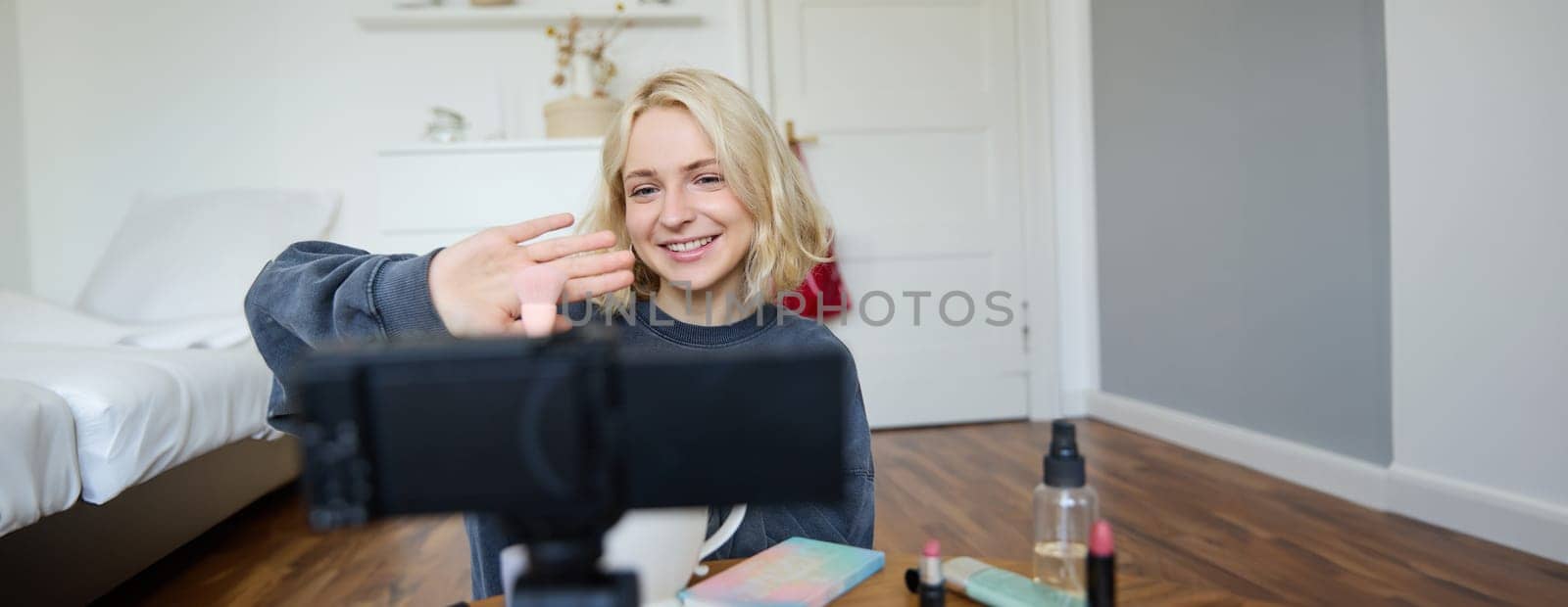 Close up portrait of happy young beauty blogger, records lifestyle vlog in her room, using camera with stabiliser, shows makeup brush and cosmetics.