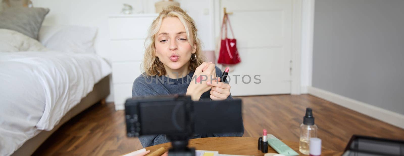 Portrait of young female blogger, beauty makeup vlogger, showing lipstick swatches on her hand, recommending cosmetics to her followers, creating content for social media account on digital camera by Benzoix