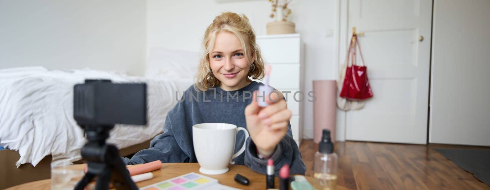 Portrait of smiling charismatic woman, puts on lip gloss, drinks tea, records video on digital camera, beauty content for social media account.