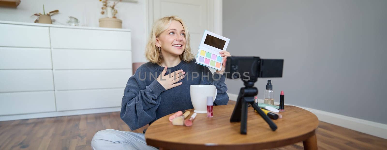 Portrait of beautiful lifestyle blogger, girl records a video on her camera for social media, shows palette of eyeshadows, does a makeup tutorial for her followers, sits in her room.