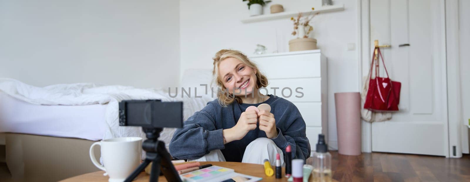 Portrait of smiling young woman, sitting in front of digital camera in cosy set up, recording video for lifestyle vlog, chatting about makeup and beauty products by Benzoix