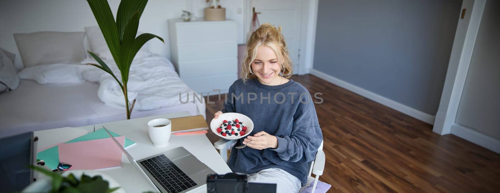 Portrait of young woman vlogger, recording herself while eating homemade healthy breakfast, creating vlog content for followers.