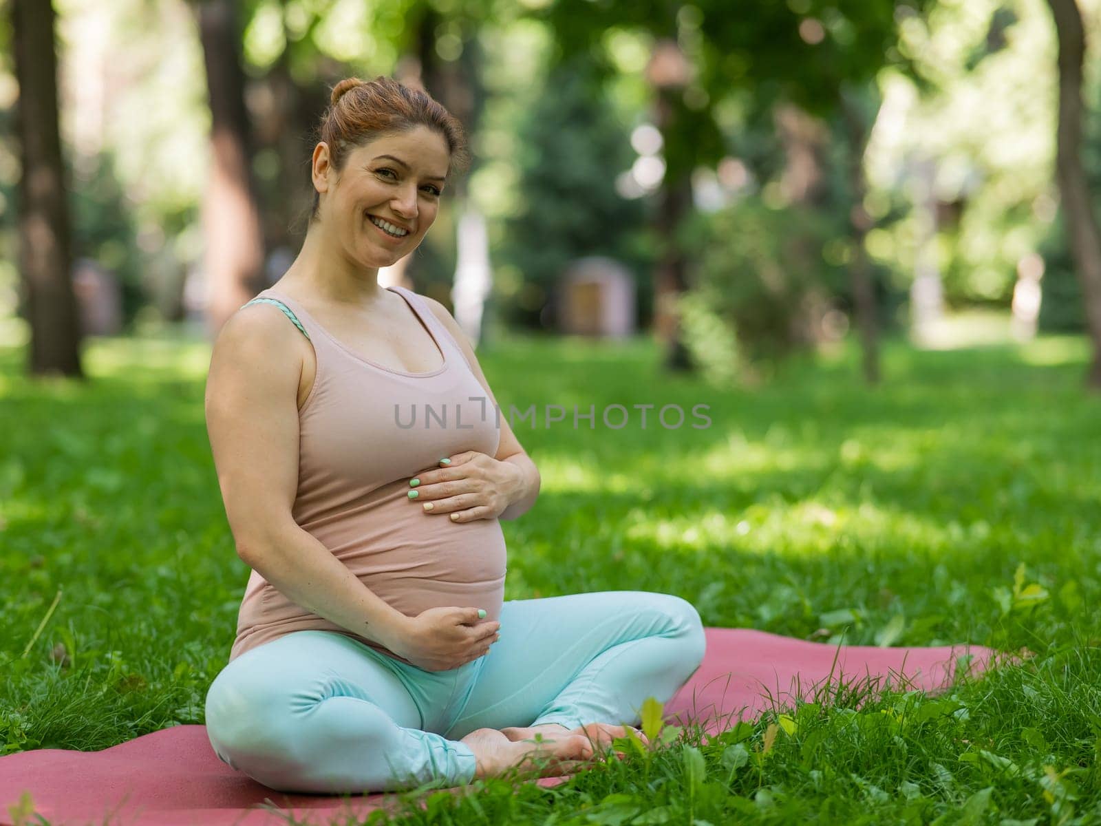 Prenatal yoga. Caucasian pregnant woman doing butterfly pose in the park