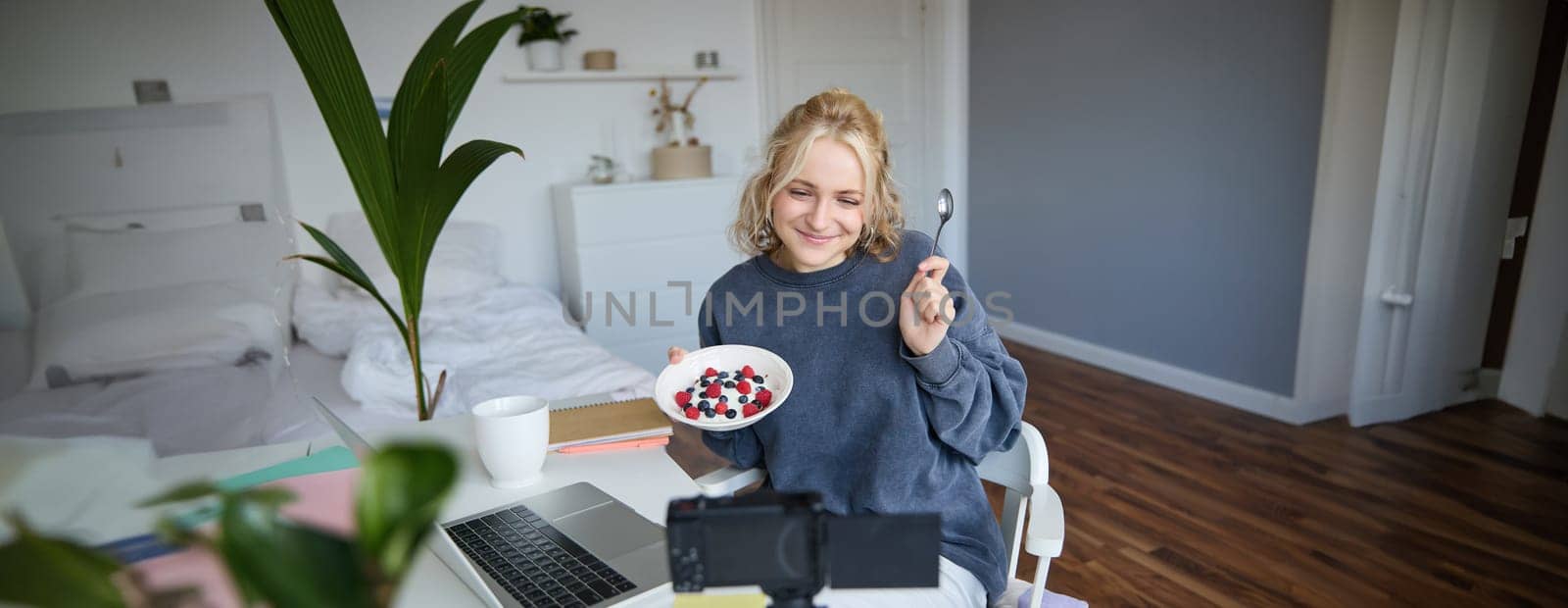 Portrait of young woman vlogger, recording herself while eating homemade healthy breakfast, creating vlog content for followers by Benzoix
