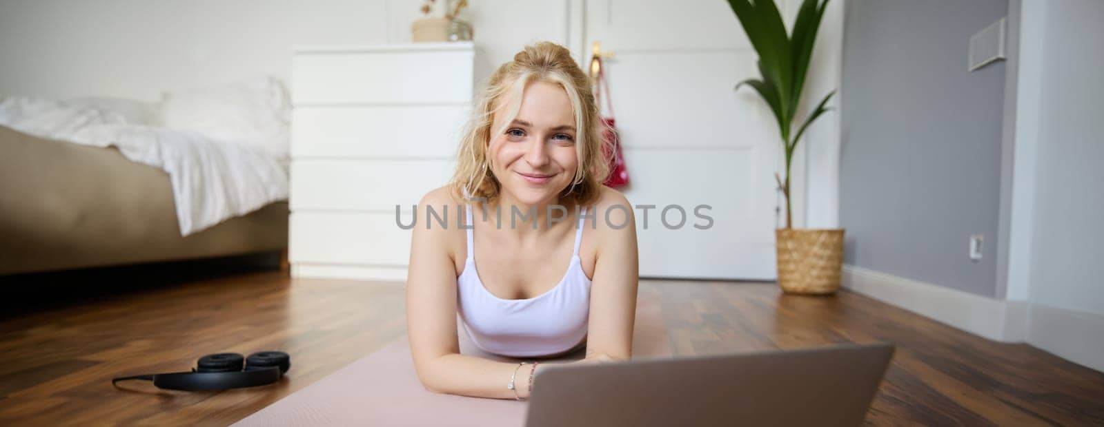 Portrait of young smiling woman doing fitness training, yoga session at home, lying on rubber yoga mat and working out by Benzoix