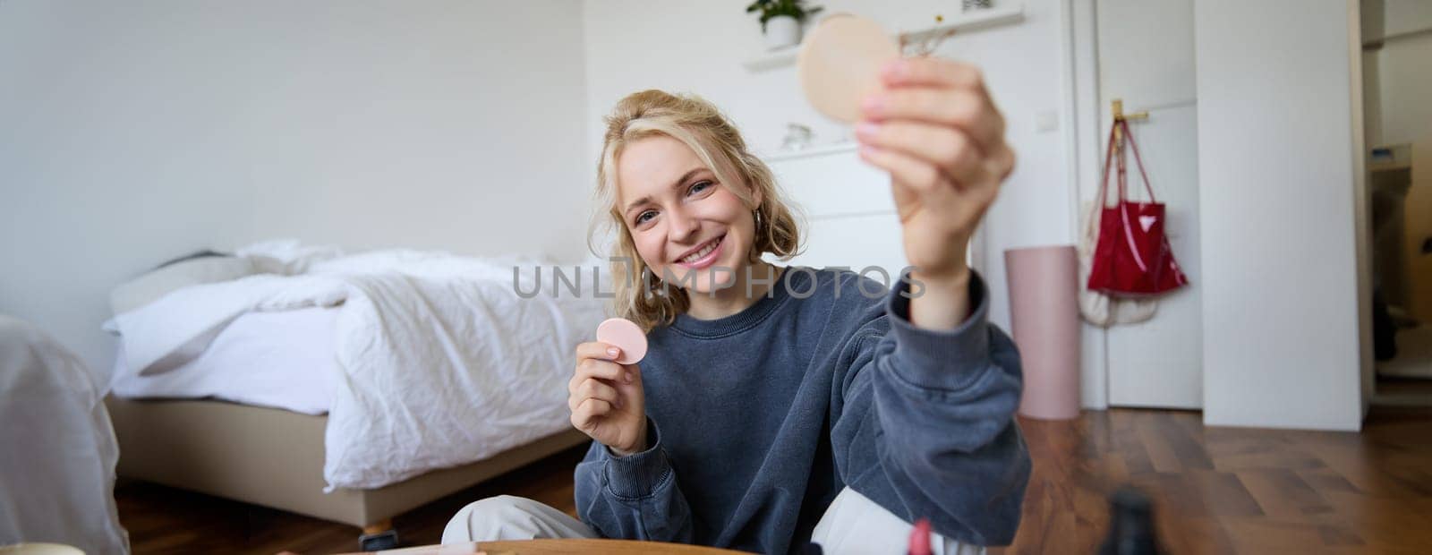 Image of young blond woman, girl records video about makeup, shows skin tone beauty products, sits in a room on floor by Benzoix