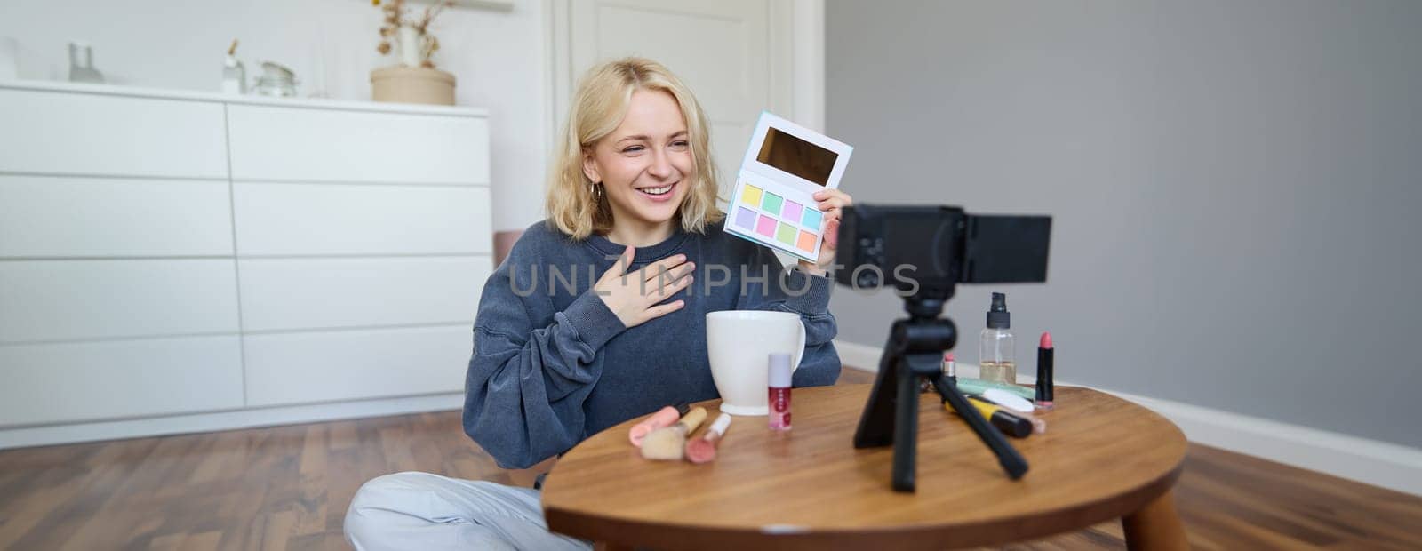 Portrait of beautiful smiling woman, recording video in her room, has camera on coffee table, reviewing makeup, doing lifestyle vlog for social media account, records a tutorial.