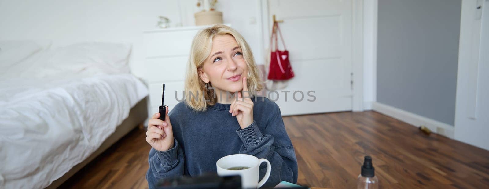 Portrait of young charismatic woman, girl records video while putting on makeup, reviewing beauty products for social media account, has a lifestyle blog, holding mascara by Benzoix