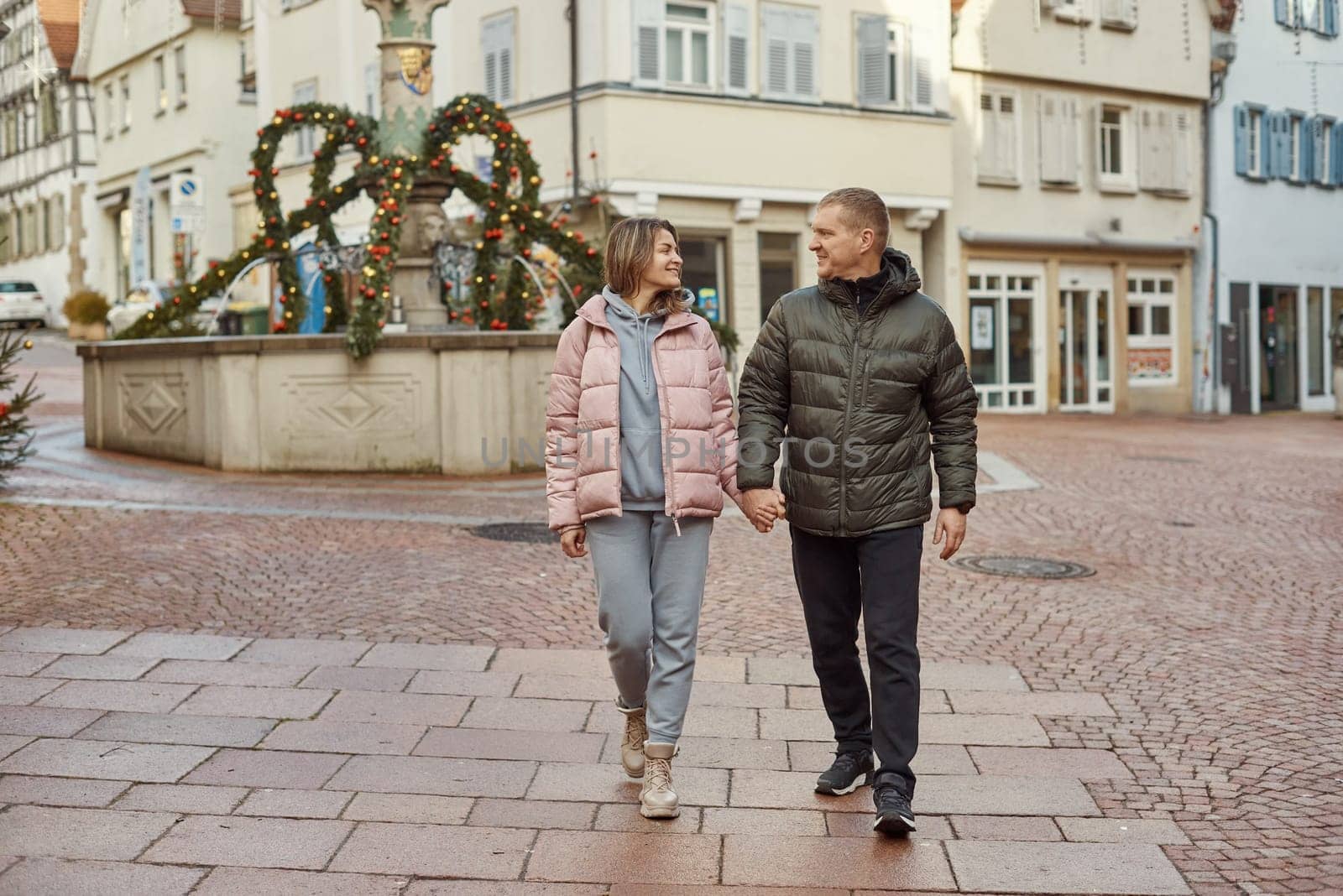 Loving couple of tourists walking around old town. Couple of lovers leisurely stroll in the cool autumn morning on the streets of a BIETIGHEIM-BISSINGEN (Germany). The guy holds his wife. Vacation, Winter, holiday. Romantic Stroll through Historic German Charm. Couple Walking in Europe's Old Town by Andrii_Ko