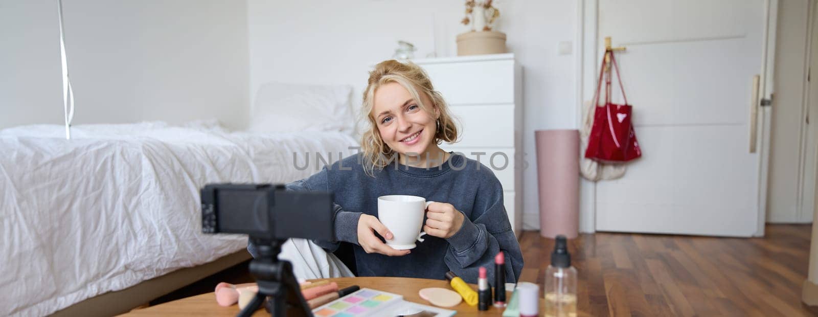 Portrait of young woman, social media influencer, blogger sitting in front of camera with cup of tea and talking, recording video in her bedroom by Benzoix