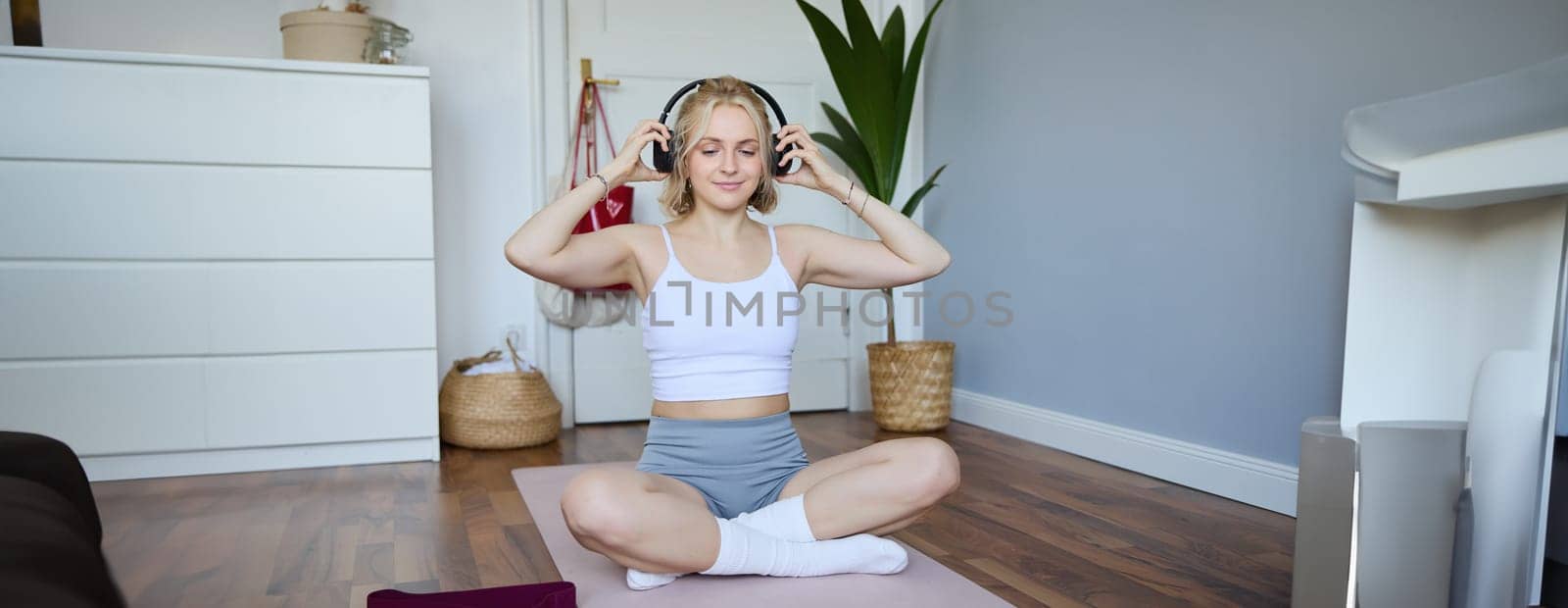 Portrait of fit and healthy young woman in wireless headphones, does workout, using online video tutorials, listens to fitness instructor on laptop, exercising at home.