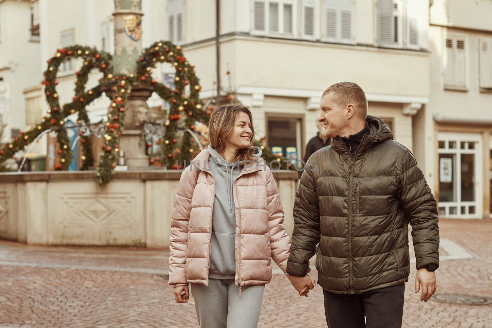 Loving couple of tourists walking around old town. Couple of lovers leisurely stroll in the cool autumn morning on the streets of a BIETIGHEIM-BISSINGEN (Germany). The guy holds his wife. Vacation, Winter, holiday. Romantic Stroll through Historic German Charm. Couple Walking in Europe's Old Town by Andrii_Ko