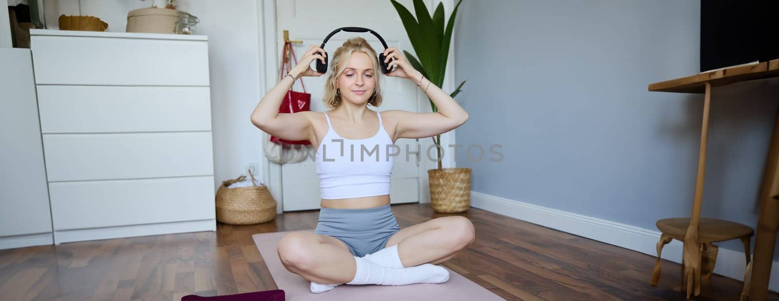 Portrait of young fitness girl, woman workout at home, listens to fitness instructor in wireless headphones, follows exercises on laptop by Benzoix