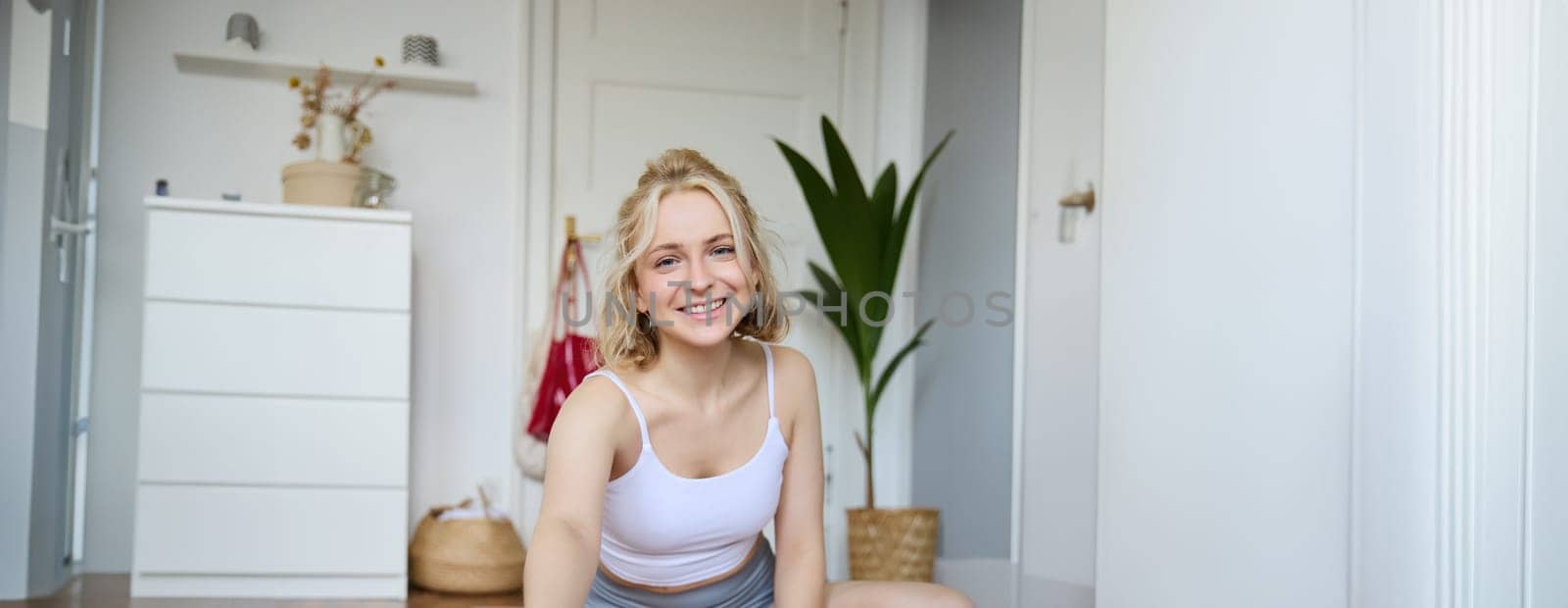 Vertical shot of athletic, fitness woman recording video of herself on digital camera, creating content for social media about workout and home exercises.