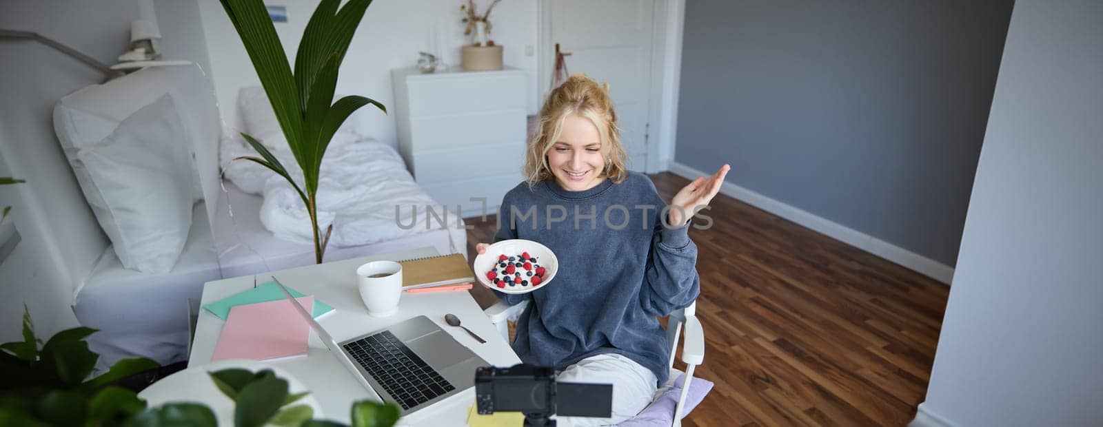 Portrait of young woman talking to audience, recording vlog on digital camera, showing her breakfast, talking about healthy food and lifestyle.