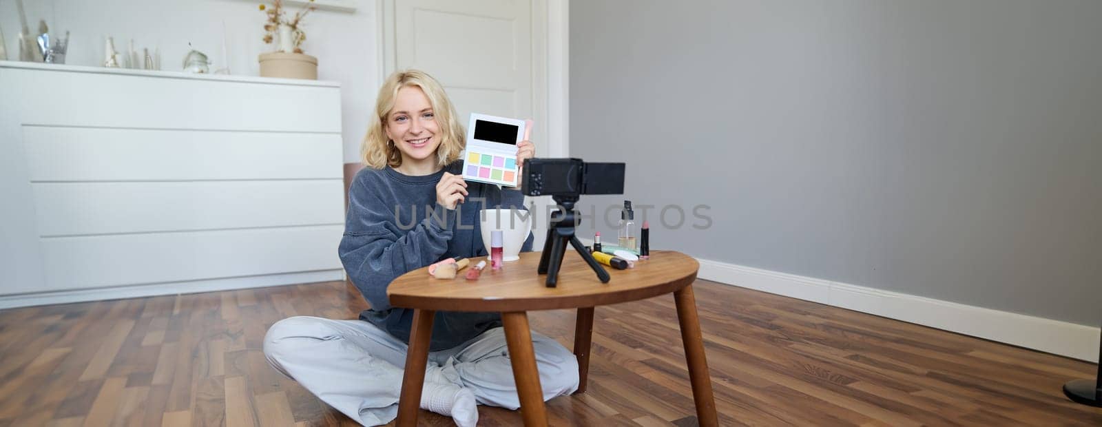 Portrait of beautiful smiling woman, recording video in her room, has camera on coffee table, reviewing makeup, doing lifestyle vlog for social media account, records a tutorial.