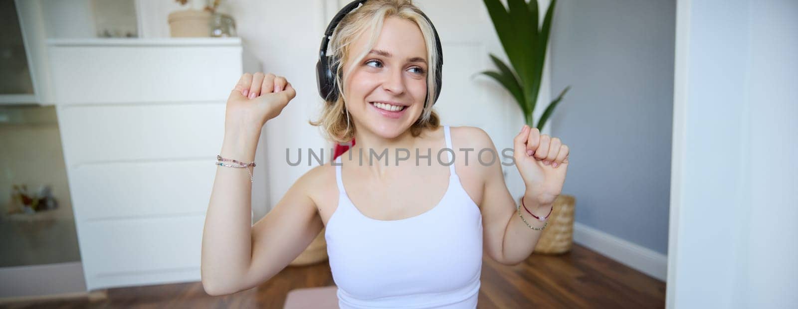 Portrait of beautiful blond girl, fitness woman dancing in wireless headphones, enjoying working out tuning into favourite song.