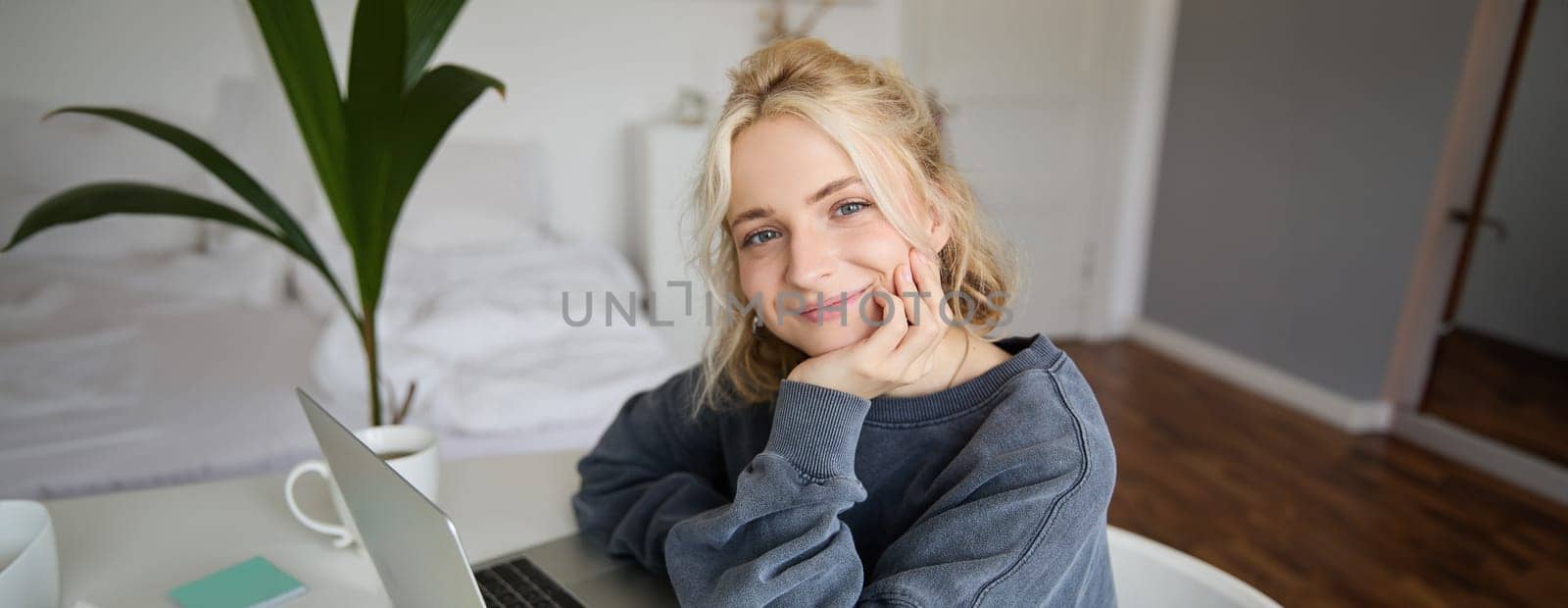 Portrait of young smiling woman, female student sitting in her room with laptop, looking cute at camera.