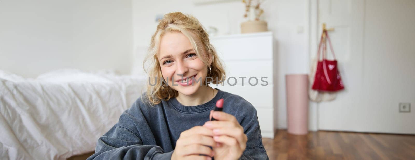Portrait of young beautiful woman, content maker creating a new vlog, beauty video, showing lipstick, recommending makeup, records a tutorial.