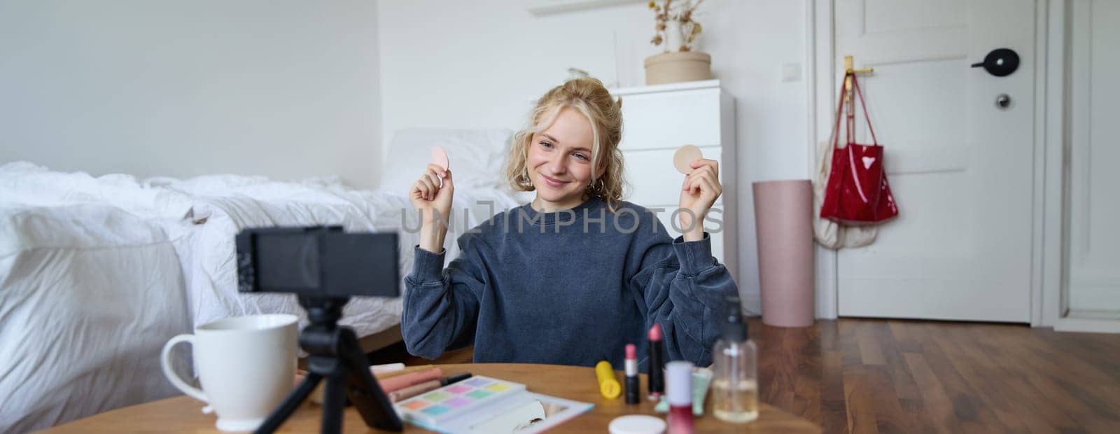 Image of young woman, vlogger records video on digital camera, shows beauty products, recommending makeup for audience on social media, sits on front in a room by Benzoix
