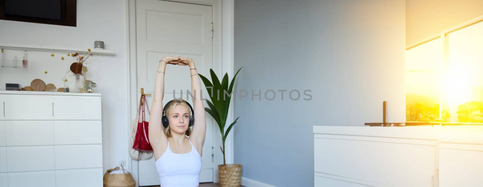 Portrait of young fitness woman doing warm-up exercises, looking at workout video on laptop, stretching arms, wearing headphones.