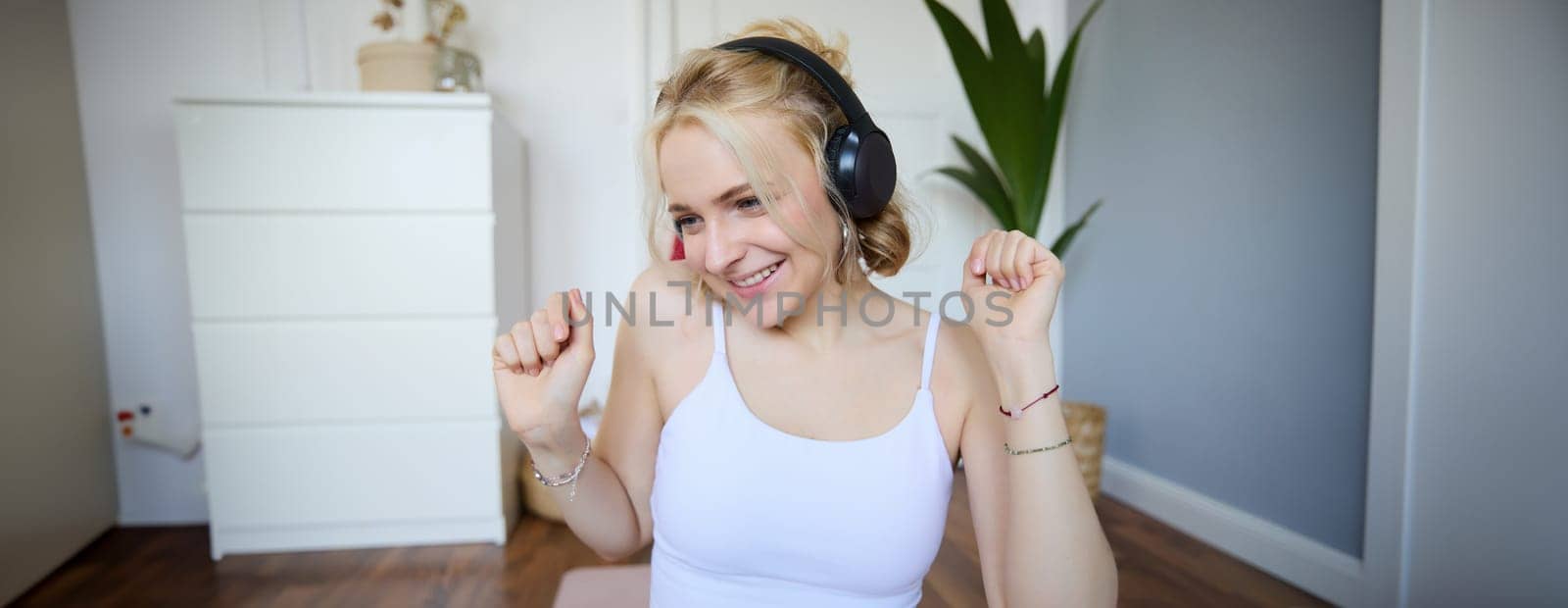 Portrait of beautiful blond girl, fitness woman dancing in wireless headphones, enjoying working out tuning into favourite song.