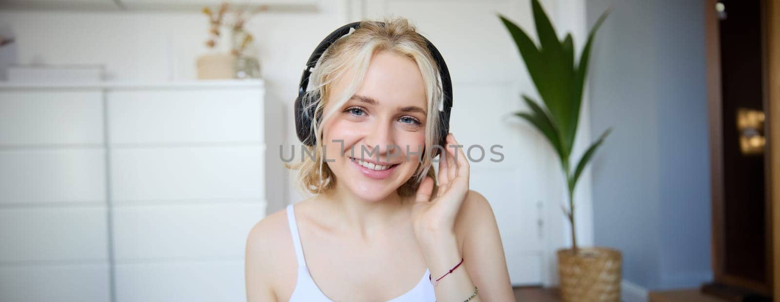 Portrait of good-looking young blond woman in wireless headphones, listens to podcast or favourite song, enjoys music in new earphones.