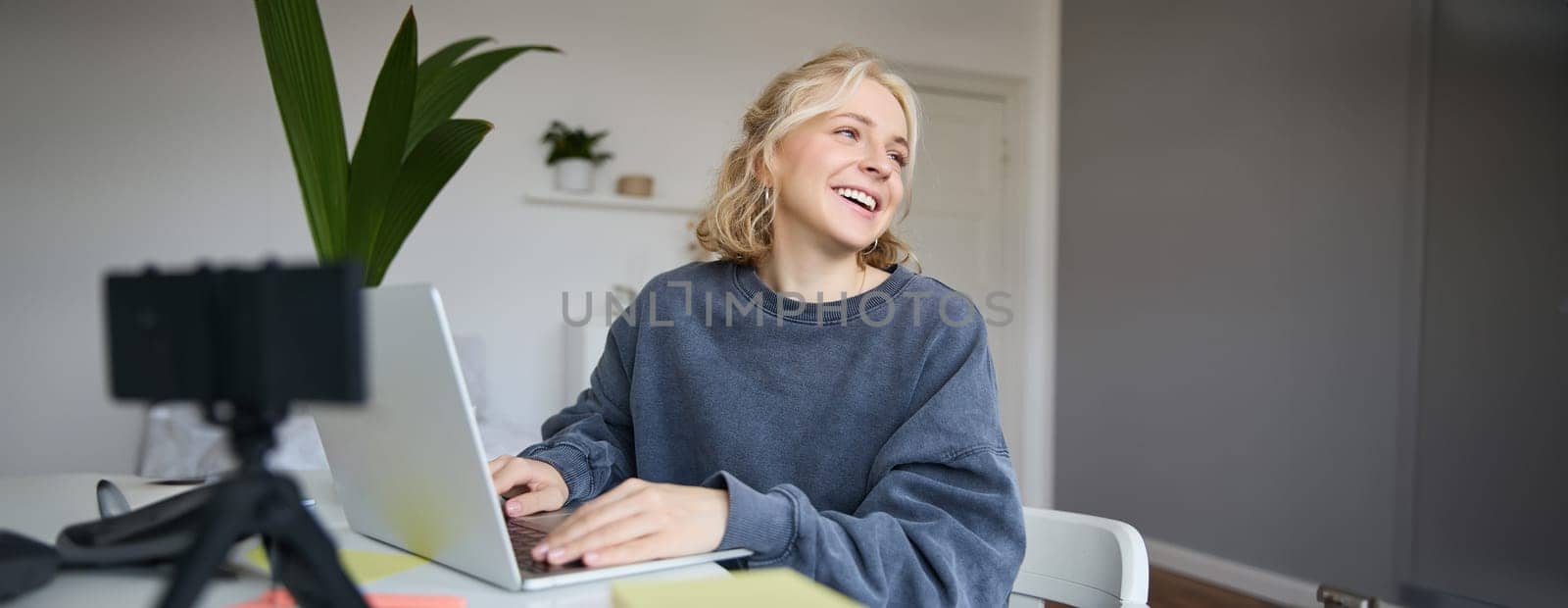 Portrait of young blond woman, female college student works from home on assignment, uses laptop, studies remotely, sits in room in front of computer by Benzoix