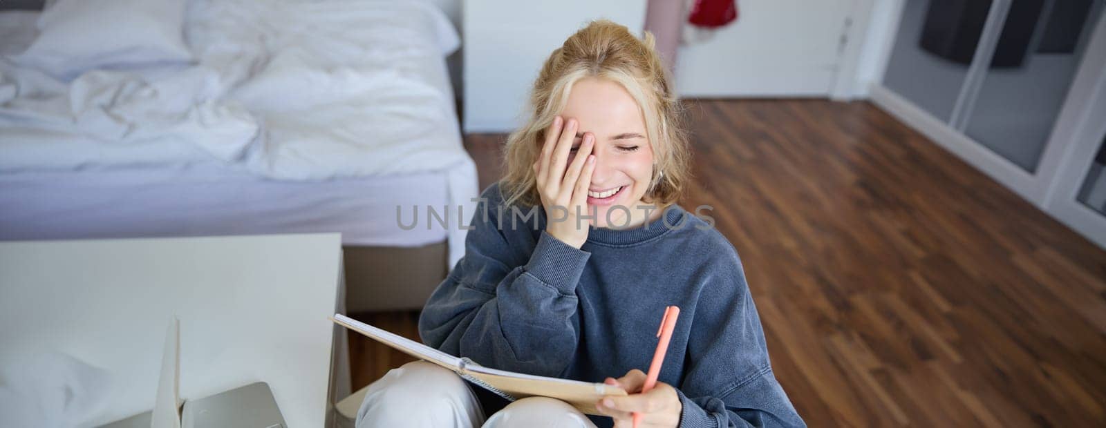 Portrait of charismatic blond girl, smiling woman in bedroom, holding notebook and pen, writing in journal or diary, creates to do list in planner.