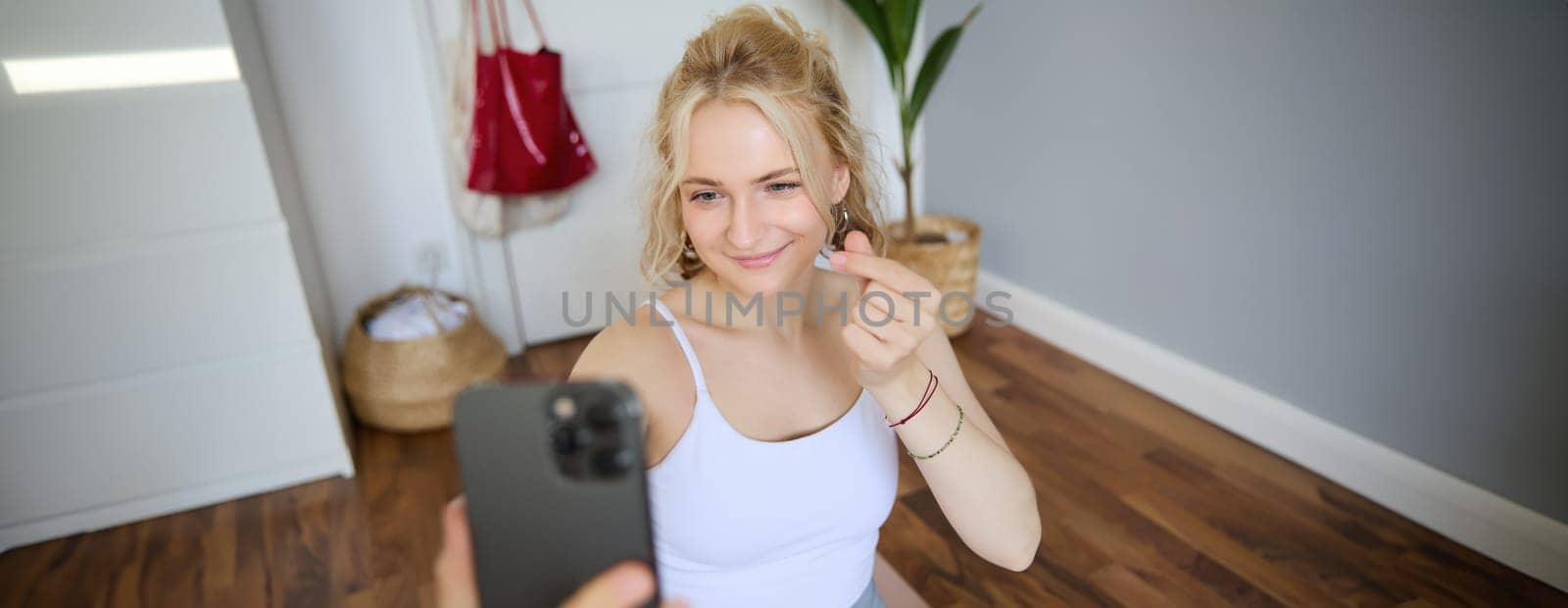 Portrait of smiling, beautiful young woman, social media content creator, takes selfies on smartphone during workout, doing exercises at home on yoga mat.