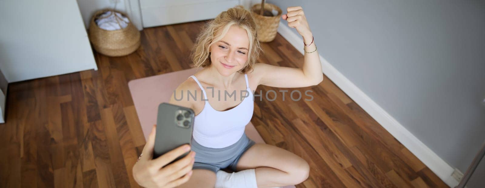 Portrait of young sporty woman taking selfie during workout training, content creator takes photos, shows muscles on camera, flexing biceps by Benzoix