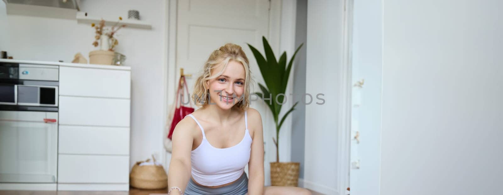 Vertical shot of woman recording her workout on digital camera, making a video about yoga and fitness at home, sitting on rubber mat in activewear by Benzoix