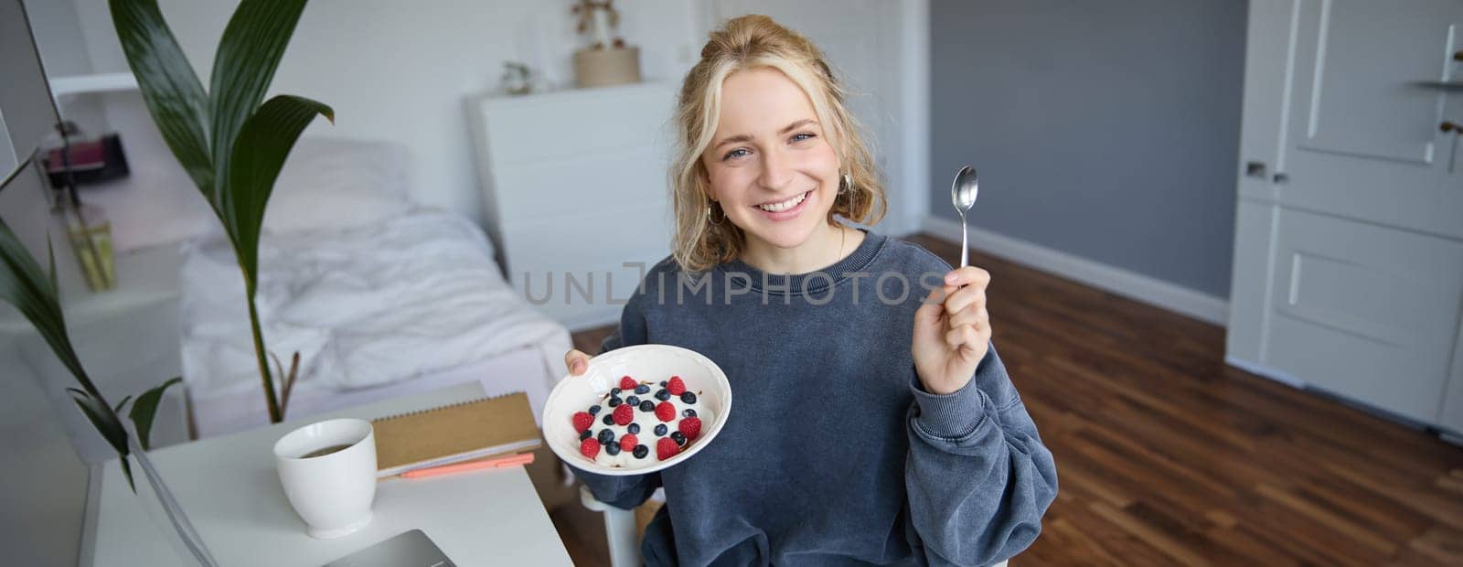 Portrait of young woman talking to audience, recording vlog on digital camera, showing her breakfast, talking about healthy food and lifestyle.