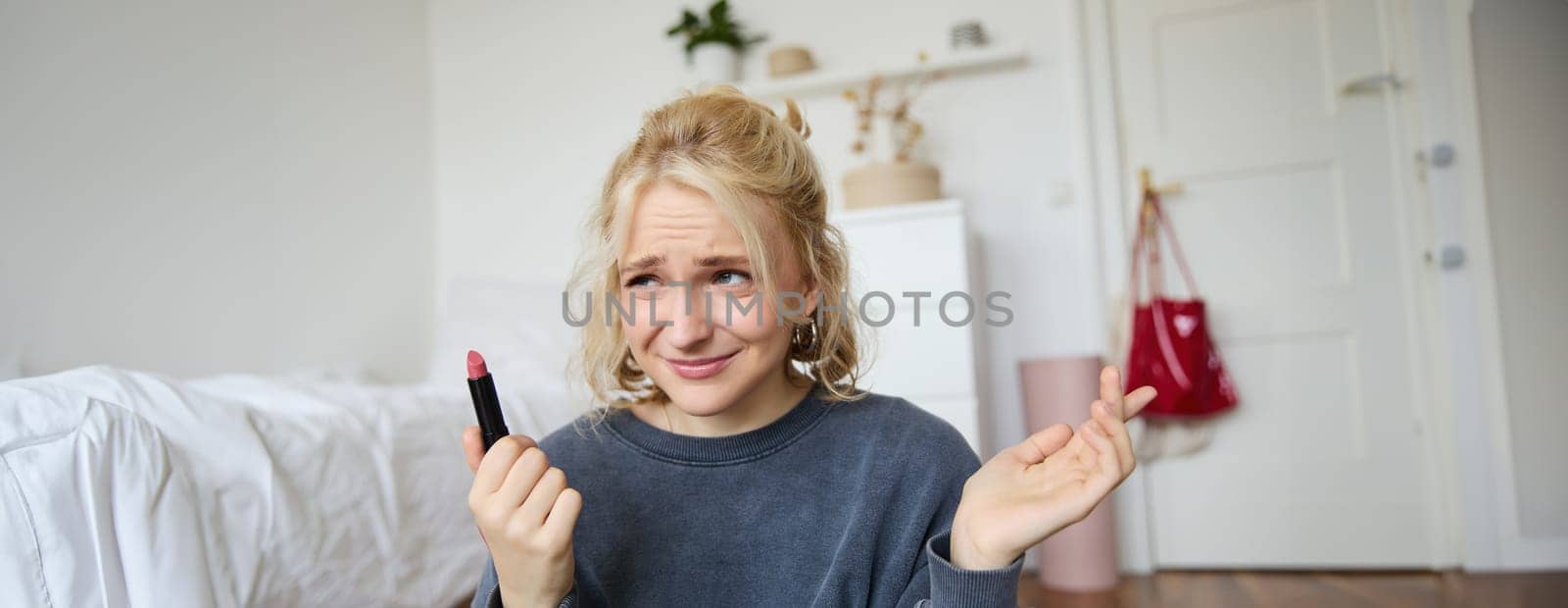 Portrait of woman, vlogger looking disappointed, showing lipstick and shrugging shoulders, recording video about makeup for social media account by Benzoix
