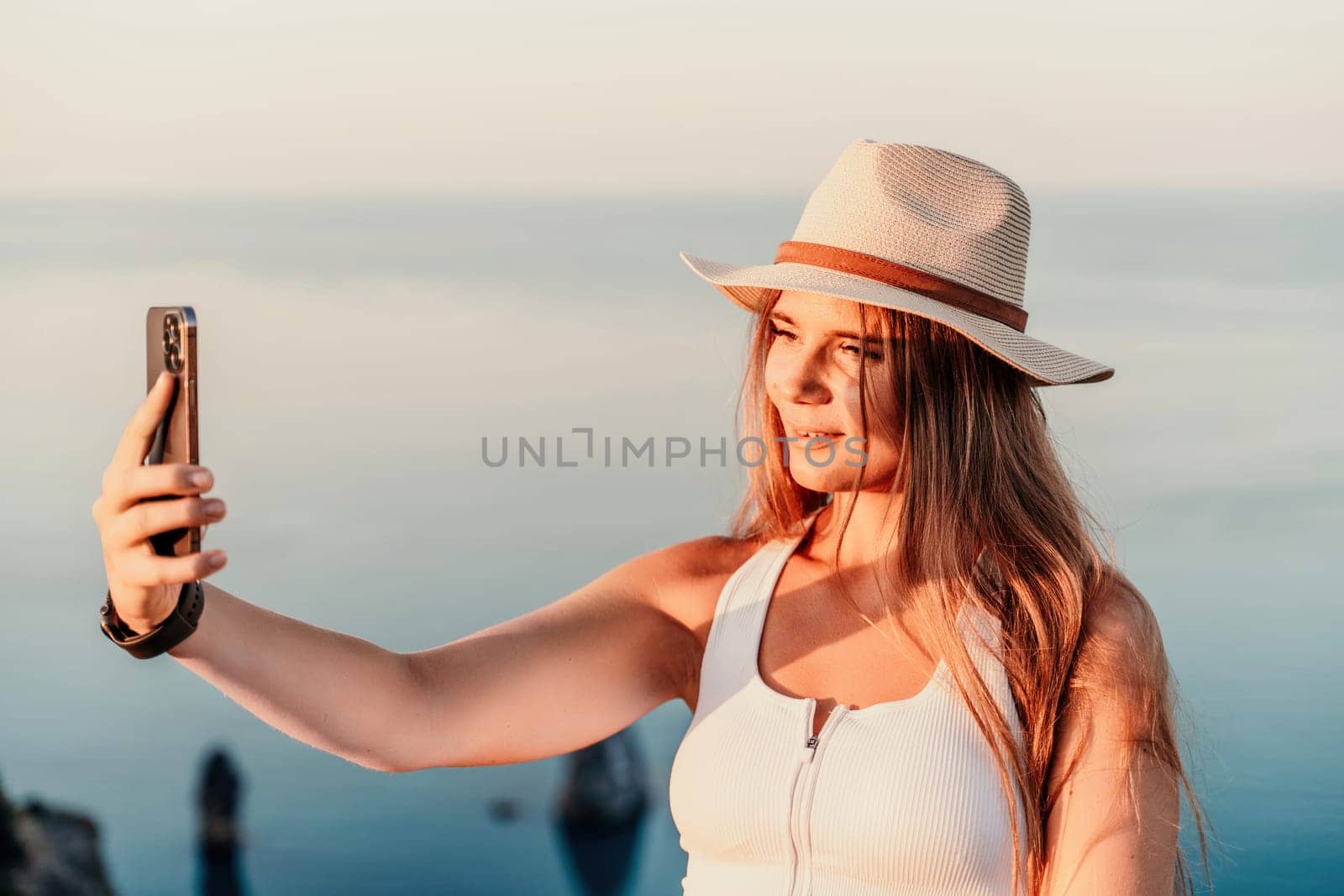 Selfie woman in hat, white tank top and shorts makes selfie shot mobile phone post photo social network outdoors on sea background beach people vacation lifestyle travel concept. by Matiunina