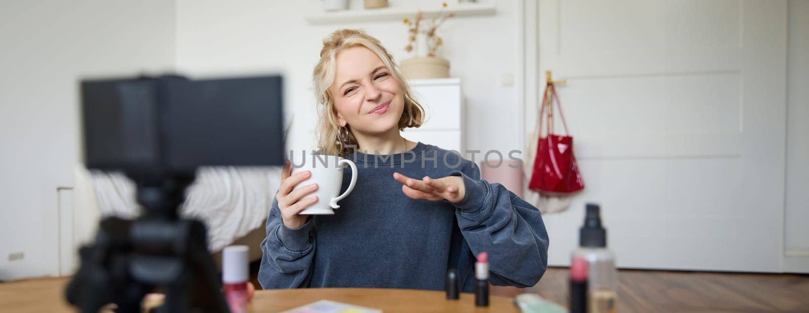 Portrait of stylish lifestyle blogger, woman talking in front of video camera, records vlog about her day in life, drinks tea and speaks to audience.