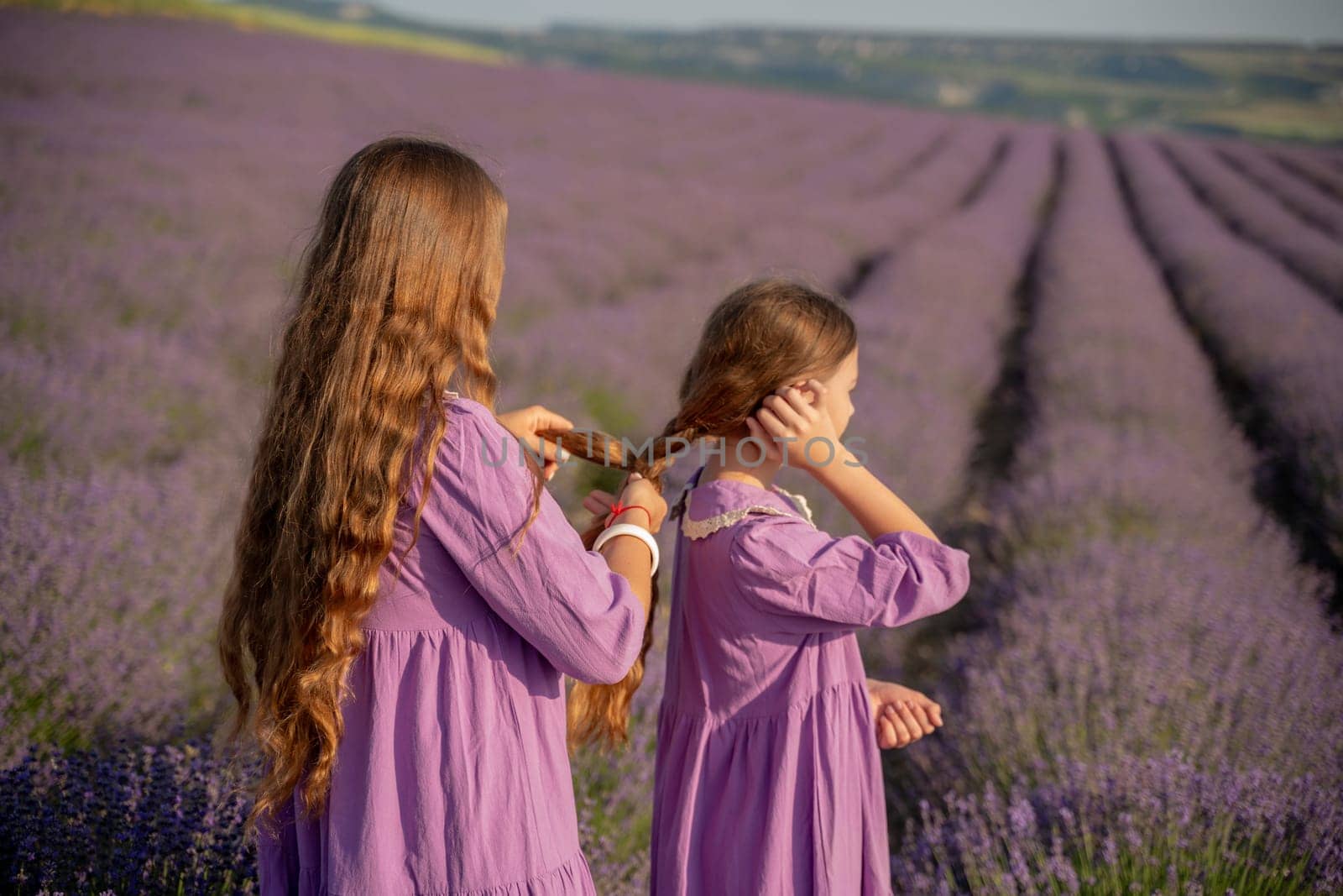 Mom and daughter braiding each other's hair in a field of lavender. The scene is peaceful and serene, with the girls enjoying each other's company and the beauty of their surroundings by Matiunina