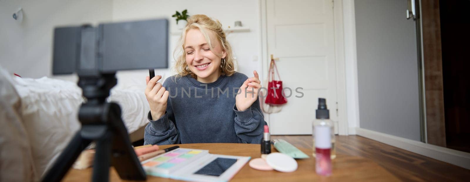 Portrait of young content maker, woman blogger recording a video on digital camera, showing lipstick colour to her followers, creating lifestyle vlog for social media account by Benzoix