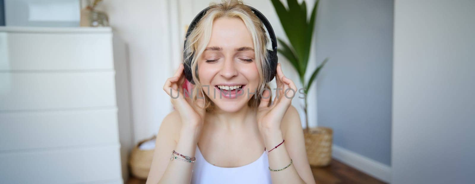 Close up portrait of woman smiling while listening to music in wireless headphones, singing with eyes closed by Benzoix