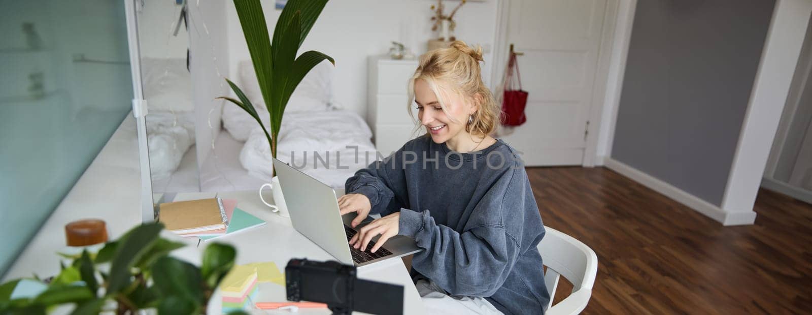 Portrait of woman sitting at desk with laptop, recording video of herself on laptop, making lifestyle video for social media account by Benzoix