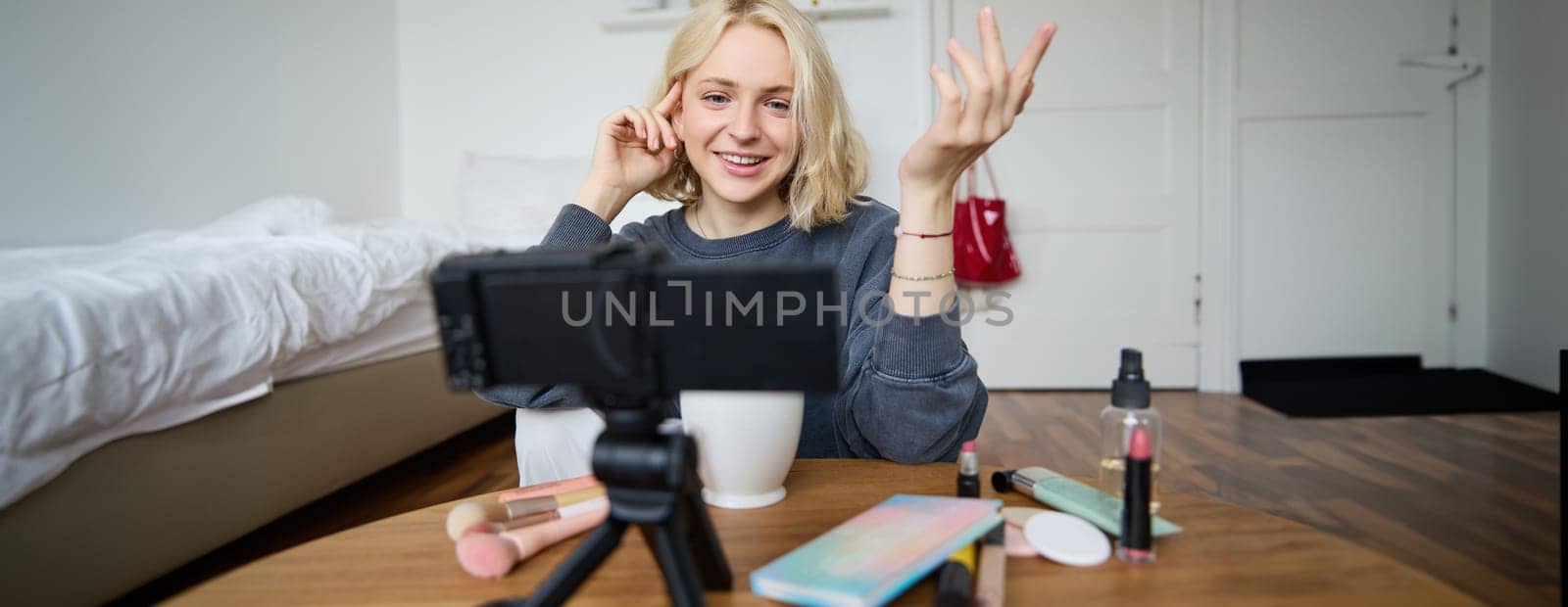 Portrait of young teenage girl in her room, recording a vlog, daily lifestyle video for social media, internet influencer advertising product online, talking to the camera, sitting on the floor.