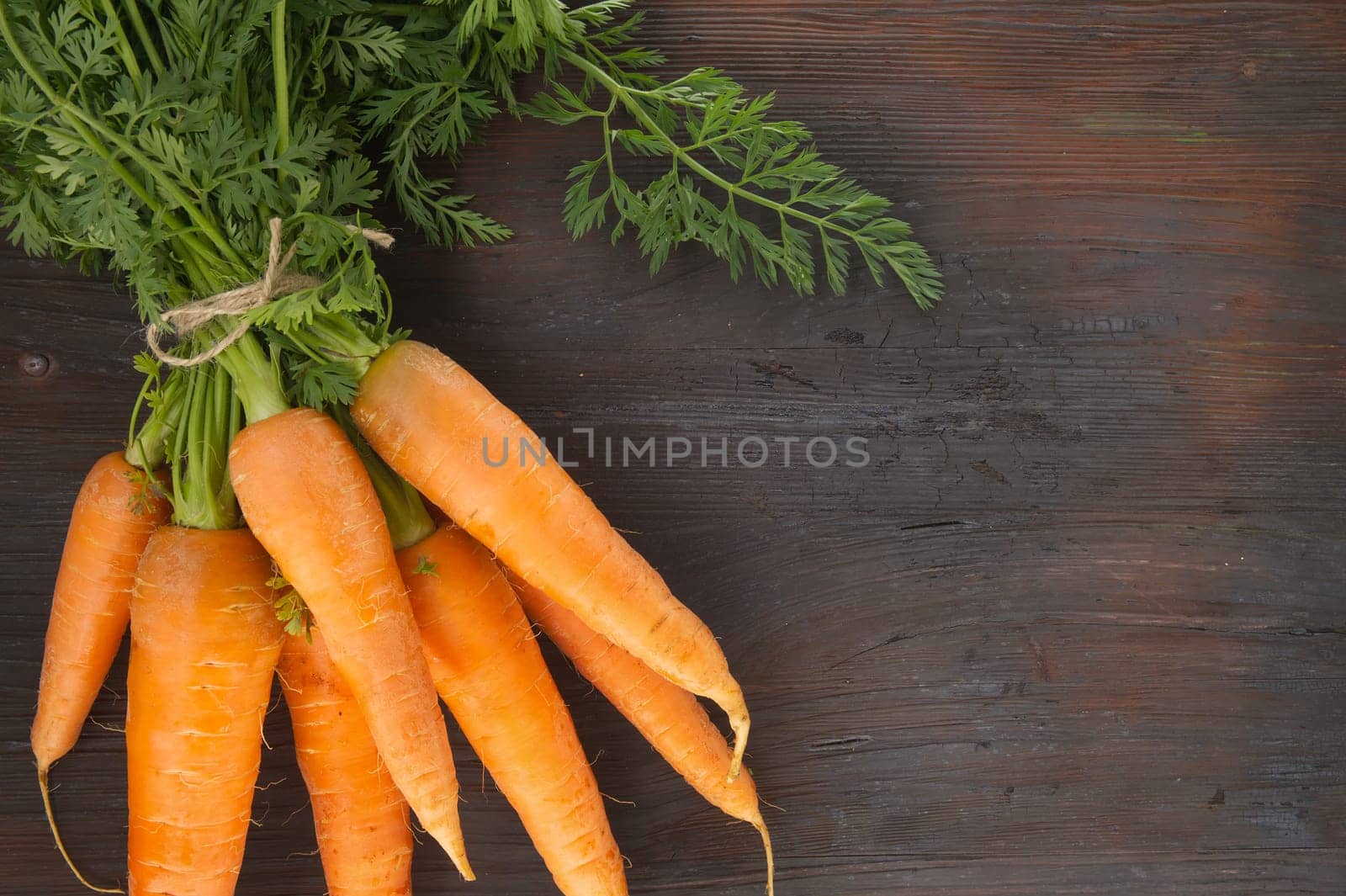 Bundle of fresh, orange carrots with green tops on wooden table by NetPix